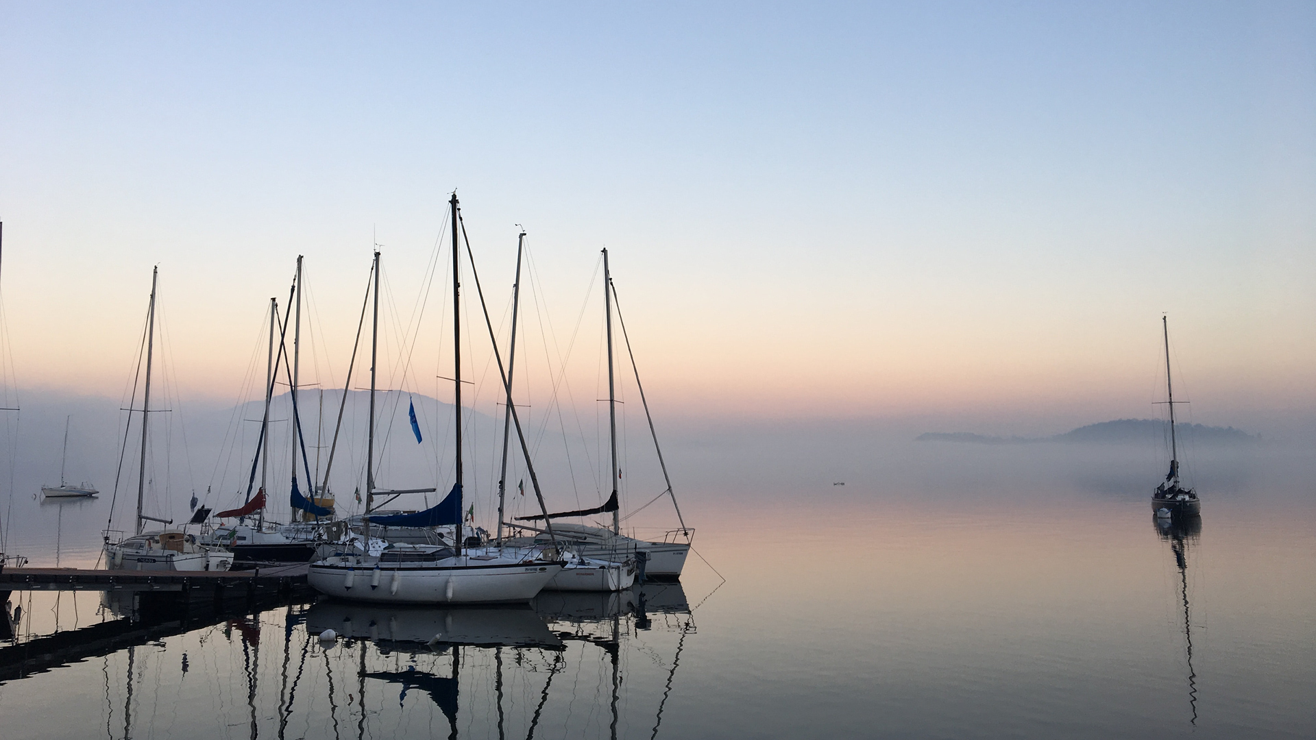 Segelboote in der Dämmerung bei Morgennebel an einem Steg.